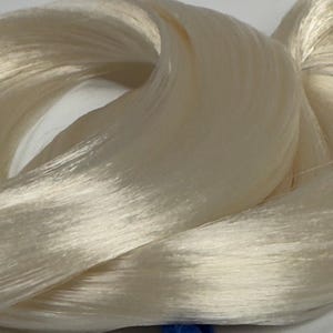 Peut inclure: Gros plan sur une botte de fil de soie ivoire. Les fils sont étroitement filés, créant une texture lisse et brillante. La soie semble douce et délicate, avec de subtiles variations de tons. Cette image met en valeur la beauté naturelle de la soie.