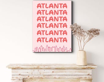 May include: A pink poster featuring the word "ATLANTA" in a bold, red font, repeated six times. A red skyline graphic is at the bottom. The poster is displayed above a wooden mantelpiece.