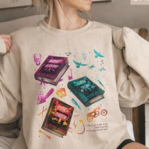 Butcher and Blackbird light blue sweatshirt featuring a vintage bookish collage for the Ruinous Love series by Brynne Weaver. Graphics include book covers for Leather and Lark and Scythe and Sparrow, a skull, motorcycle, and chainsaw. Aesthetic dark romance reader crewneck pullover in a soft pastel blue tone.