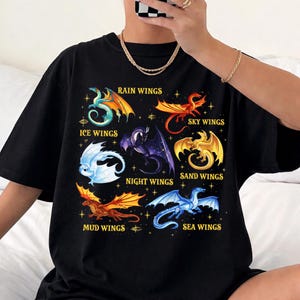 May include: Black t-shirt with vibrant dragon designs, showcasing different wing types such as "Rain Wings" and "Sky Wings." The artwork includes text and star details, creating a fantasy theme.