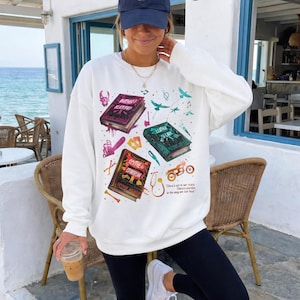 Butcher and Blackbird sand-colored sweatshirt featuring a vintage bookish collage for the Ruinous Love series by Brynne Weaver. Graphics include book covers for Leather and Lark and Scythe and Sparrow, a skull, motorcycle, and chainsaw. Aesthetic dark romance reader crewneck pullover in a neutral beige tone.