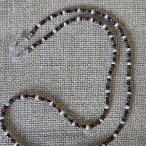 May include: Eyeglass chain with a beaded design. The chain features small, round beads in white, brown, and black, strung together to create a decorative and functional accessory. The chain has silver-colored loops for attaching to glasses.