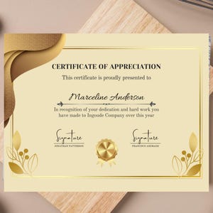 Pode incluir: Um certificado de apreço com um esquema de cores dourado e creme. O texto diz "CERTIFICATE OF APPRECIATION" e é apresentado a "Marceline Anderson". Inclui assinaturas e um selo dourado. O certificado está em uma superfície de madeira.
