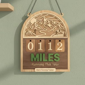 May include: Wooden running tracker with a mountain scene cutout. The tracker displays "0112 MILES Running This Year" with a personalized name at the bottom. It hangs from a chain and has a natural wood finish.