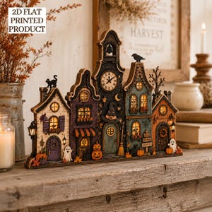 May include: A 2D flat printed Halloween village display featuring a row of interconnected houses with a central clock tower, decorated with pumpkins, ghosts, a black cat, a witch hat, and a broom, with the text 2D FLAT PRINTED PRODUCT visible.