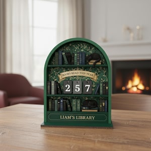 Puede incluir: Una estantería de madera verde con el texto "BOOKS READ THIS YEAR" y "LIAM'S LIBRARY". La estantería muestra el número "257" y tiene libros en miniatura y figuras de gatos negros. El fondo presenta un patrón floral.