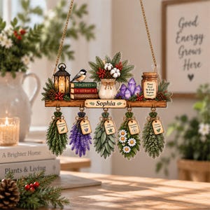 May include: A hanging wooden sign personalized with the name Sophia, featuring a lantern, a bird, books labeled Plants, Herbs, Happiness, a vase with cotton, purple crystals, and a jar labeled Plant Heal Be Kind Repeat, with five hanging herb bundles.