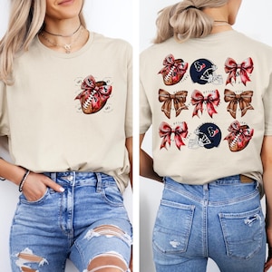 May include: Beige t-shirt with a football and red bow design on the front. The back features a pattern of footballs, helmets, and bows. The shirt is worn with blue jeans. The design includes the text "DESIGN".