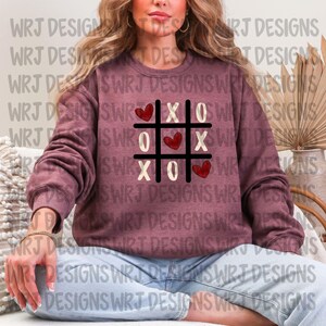 Può includere: Felpa bordeaux con un design a tris in cui i cuori sostituiscono le X e gli O. Ha girocollo e maniche lunghe. Il design è in nero, bianco e rosso. Tema di San Valentino.