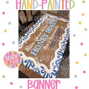 May include: A rectangular banner with a brown center and a blue and white decorative border. The text reads: Alex found her HONEY HONEY, Alex's Bachelorette, BAY ST. LOUIS. Graphics include a disco ball, two rings, and two champagne glasses.