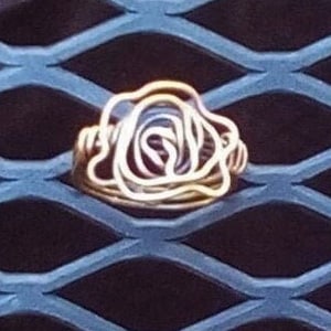 May include: A gold wire rose ring. The ring is made of thin wire that is twisted and shaped into a rose. The rose is a simple design with a few petals.