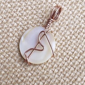 Peut inclure: Un pendentif en coquille blanche avec un motif en fil de cuivre. Le pendentif est sur un fond en toile de jute.