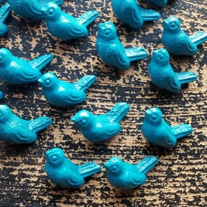 May include: A collection of teal blue bird figurines with various poses. The birds are made of a smooth, ceramic material and have a glossy finish.