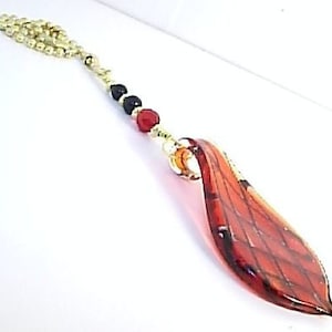May include: A red and gold beaded chain with a red and black glass pendant shaped like a leaf. The pendant has a checkered pattern.