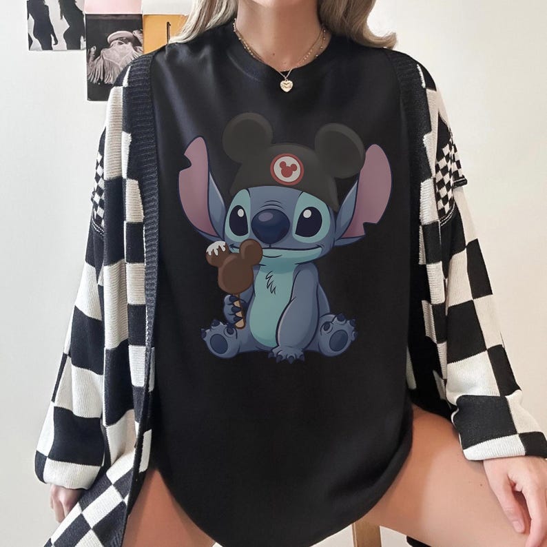 May include: Black graphic tee featuring Stitch from Lilo & Stitch wearing a Mickey Mouse hat and holding a brown ice cream bar. The tee is paired with a black and white checkered cardigan.