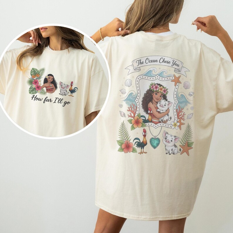 May include: Cream-coloured t-shirt with a colourful graphic from a popular animated film. The front design includes a character, a pig, and a rooster with the text "How far I'll go." The back design has the text "The Ocean Chose You."