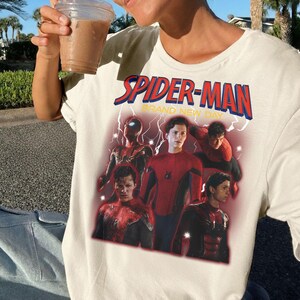 May include: Off-white t-shirt with a Spider-Man graphic and the text "SPIDER-MAN BRAND NEW DAY" in red and blue. The design showcases several images of Spider-Man in different action poses.