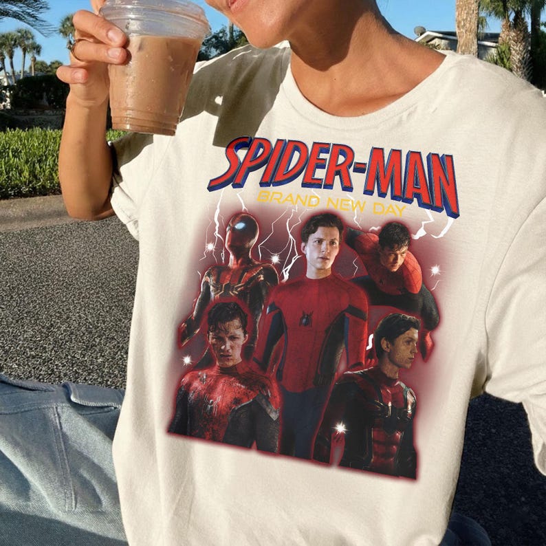 May include: Off-white t-shirt with a Spider-Man graphic and the text "SPIDER-MAN BRAND NEW DAY" in red and blue. The design showcases several images of Spider-Man in different action poses.