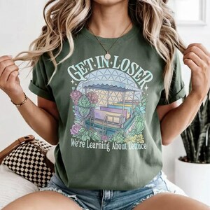 Puede incluir: Camiseta verde con el texto "GET IN LOSER" sobre una ilustraci&oacute;n de un paseo en barco con el texto "We're Learning About Lettuce". El dise&ntilde;o utiliza colores pastel.
