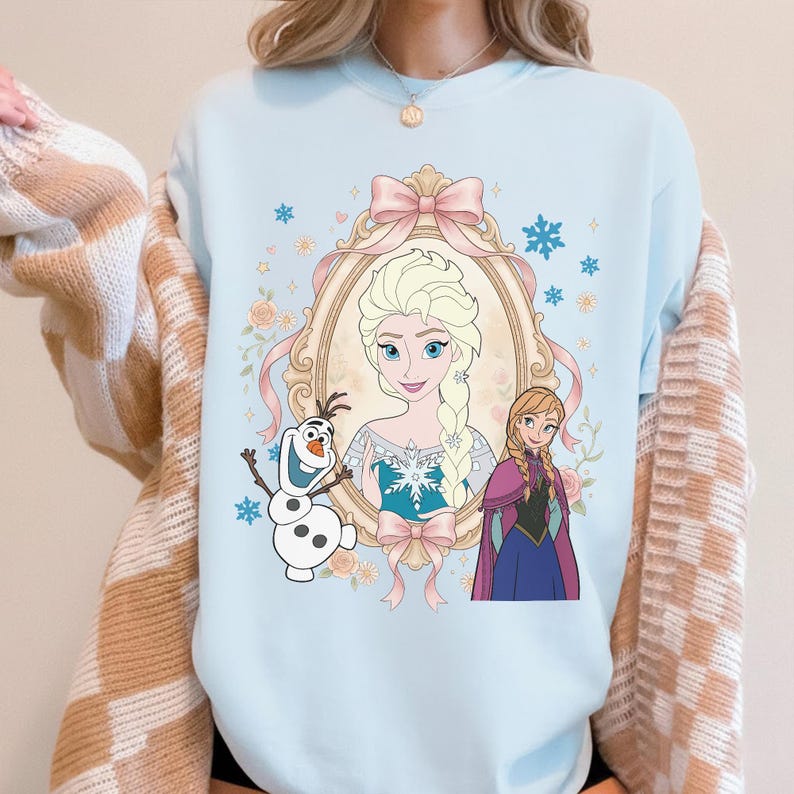 Pu&ograve; includere: Felpa azzurra con un'illustrazione incorniciata di Elsa e Anna di Frozen, con Olaf il pupazzo di neve. Il design include fiocchi rosa, accenti floreali e dettagli a fiocco di neve, creando un'estetica stravagante e incantevole.