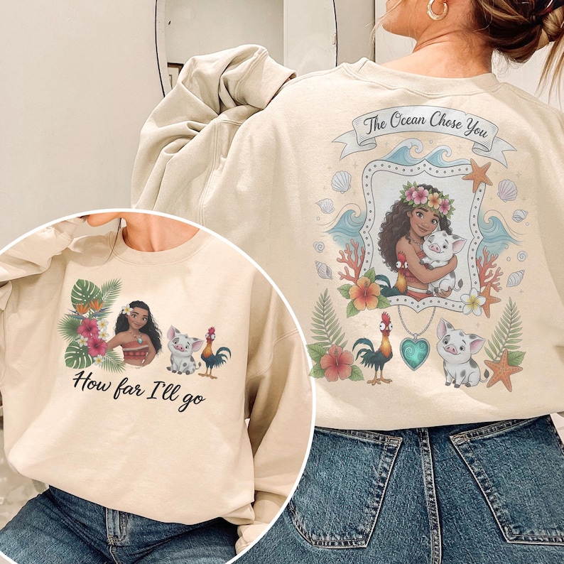 May include: Cream-coloured sweatshirt with a vibrant graphic of a woman with a flower crown, holding a pig, and the text "The Ocean Chose You". The front has the text "How far I'll go" and a matching graphic.