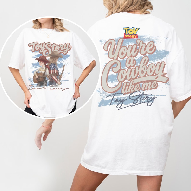 Puede incluir: Una camiseta blanca con un estampado gr&aacute;fico que incluye el texto Toy Story, You're a Cowboy like me y Tay Story. El dise&ntilde;o presenta ilustraciones de dos figuras con sombreros de vaquero, una de ellas tocando la guitarra, sobre un fondo azul.