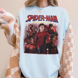 May include: Pale blue Spider-Man graphic t-shirt. The design includes the words "SPIDER-MAN BRAND NEW DAY" in red and yellow. The graphic features several images of Spider-Man in different poses.