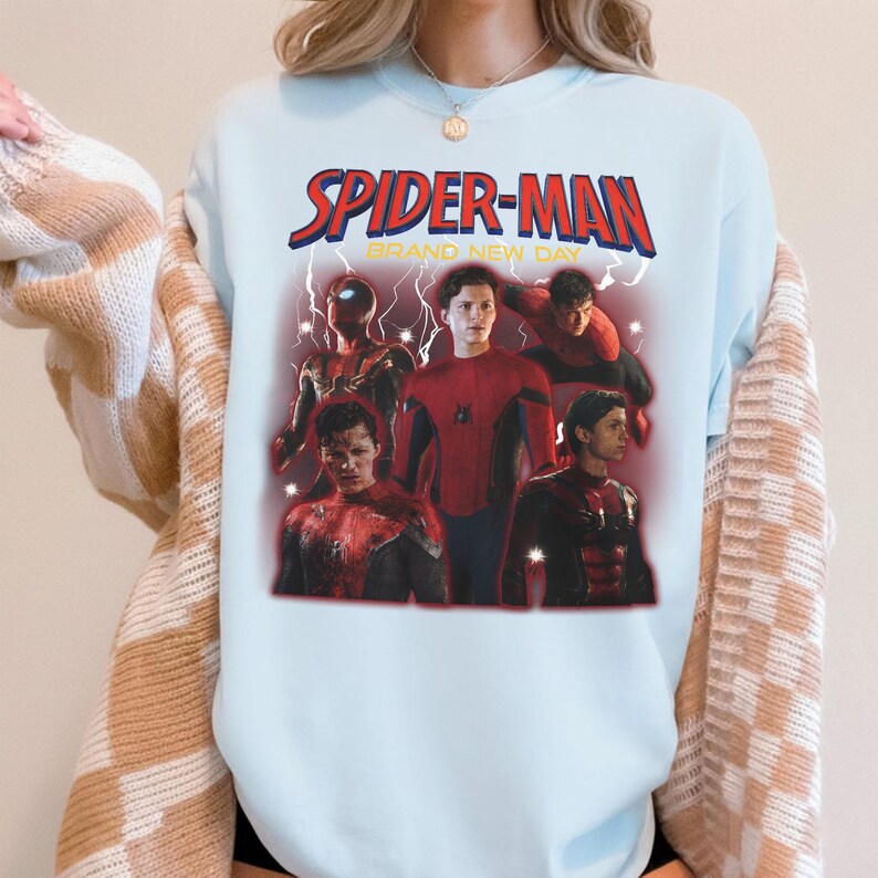 May include: Pale blue Spider-Man graphic t-shirt. The design includes the words "SPIDER-MAN BRAND NEW DAY" in red and yellow. The graphic features several images of Spider-Man in different poses.