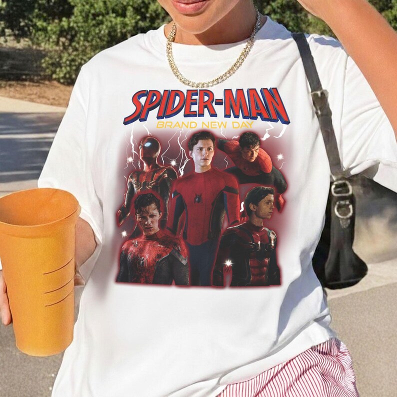 May include: White t-shirt with a graphic of Spider-Man and the text "SPIDER-MAN BRAND NEW DAY" in red and blue. The graphic features multiple images of Spider-Man in different poses and costumes.