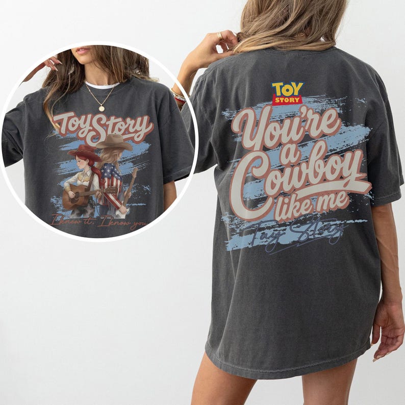 Puede incluir: Una camiseta gris carb&oacute;n con un gr&aacute;fico de Toy Story. La parte posterior muestra el texto 'You're a Cowboy like me' en letra grande sobre un trazo azul. El recuadro frontal muestra dos personajes con guitarras y el texto 'Toy Story'.