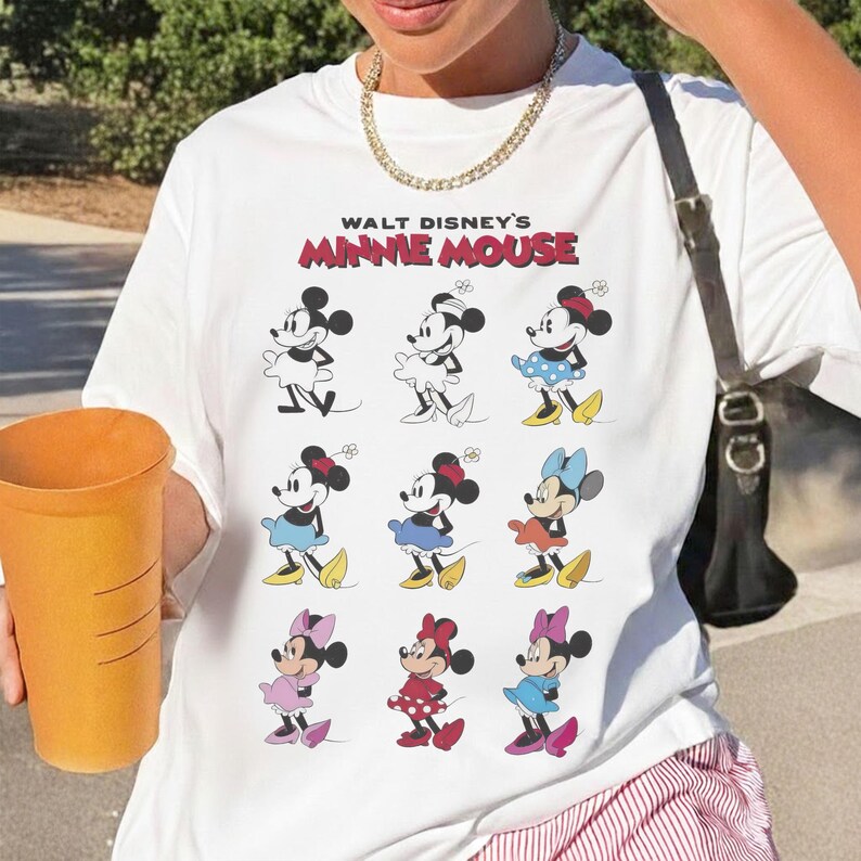 K&ouml;nnte beinhalten: Wei&szlig;es T-Shirt mit einem Aufdruck von Minnie Mouse in verschiedenen Outfits. Der Text "WALT DISNEY'S MINNIE MOUSE" ist in Rot und Schwarz aufgedruckt. Das T-Shirt hat einen Rundhalsausschnitt und einen l&auml;ssigen Stil.