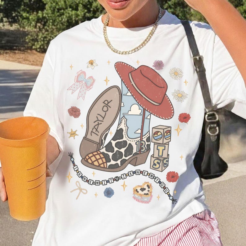 May include: A white t-shirt featuring a graphic print of a cowboy boot with a cow print pattern, a red hat, the name Taylor, the number 13, stacked blocks with letters, a beaded string with text, and various floral and star icons.