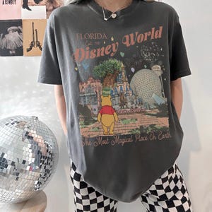 Puede incluir: Camiseta gris oscuro con un gr&aacute;fico colorido de Disney World en Florida. El dise&ntilde;o incluye el texto "Florida Disney World Est. 1971" y una imagen de Winnie the Pooh. La frase "The Most Magical Place On Earth" tambi&eacute;n est&aacute; impresa en la camiseta.