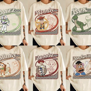 May include: Cream-colored t-shirts featuring cartoon characters Buzz, Woody, Rex, Slinky, Jessie, and Mr. Potato Head. Each shirt has a unique design with the character's name and the year 1995 in a retro style.