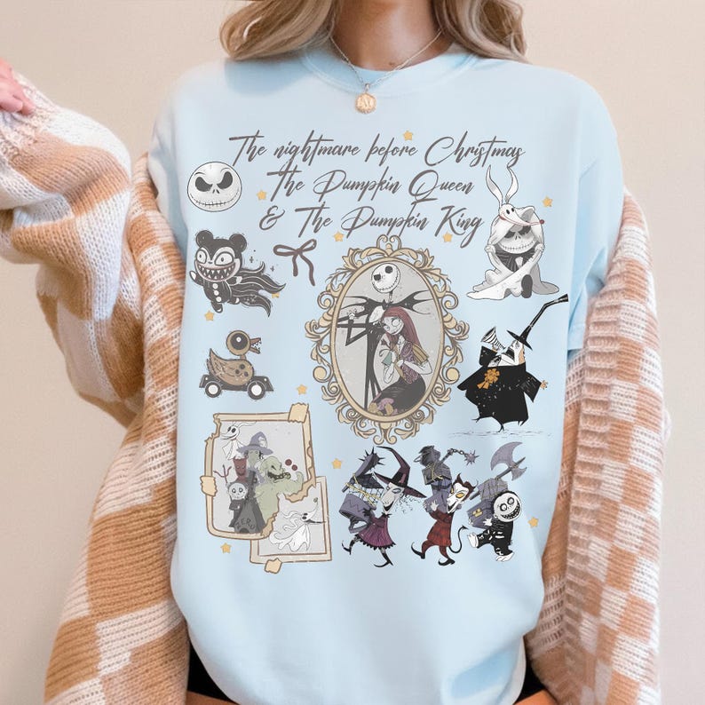May include: Pale blue sweatshirt with a design from "The Nightmare Before Christmas." The graphic includes Jack Skellington, Sally, and other characters in a collage. The text reads "The Nightmare Before Christmas & The Pumpkin Queen & The Pumpkin King."
