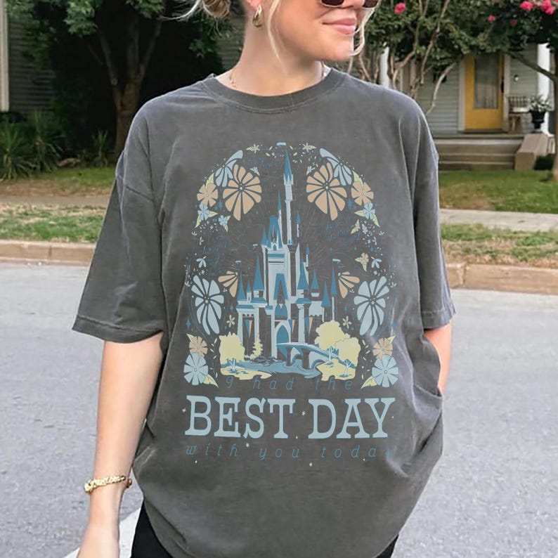May include: Dark gray t-shirt featuring a castle design with floral accents in blue, tan, and white. The text "I had the BEST DAY with you today" is printed below the castle image. The shirt has short sleeves.