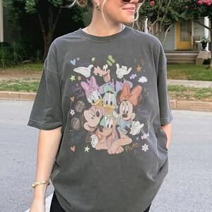 May include: Dark gray t-shirt featuring a colorful graphic of Disney characters including Mickey Mouse, Minnie Mouse, Donald Duck, Daisy Duck, and Pluto. The design includes stars, hearts, and the words "Minnie Mouse" and "Daisy Duck".