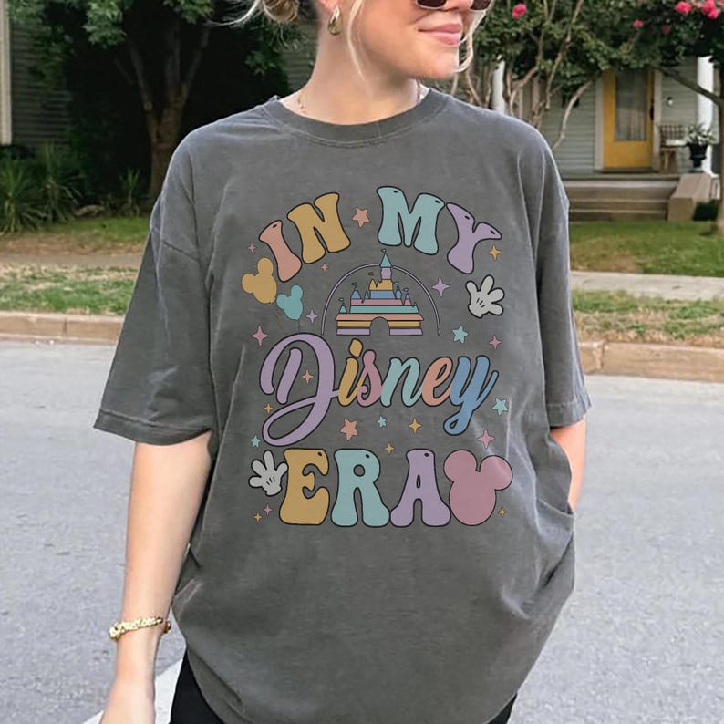Op de afbeelding: Donkergrijs T-shirt met de tekst "IN MY Disney ERA" in kleurrijke, retro letters. Het ontwerp bevat een kasteel, Mickey Mouse oren en sterren, wat een vintage thema oproept.