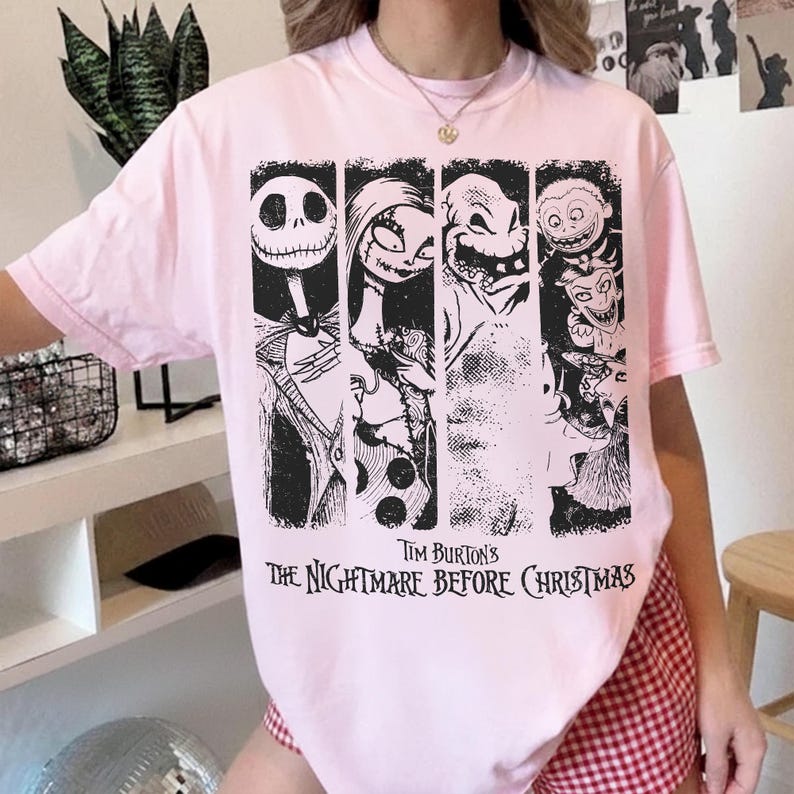 May include: A light pink short-sleeve t-shirt featuring a black and white graphic print of characters from Tim Burton's The Nightmare Before Christmas. The design includes four vertical panels showing Jack Skellington, Sally, Oogie Boogie, and Lock, Shock, and Barrel.