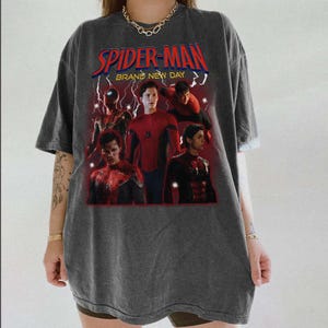 May include: Dark grey t-shirt with a Spider-Man graphic and the text "SPIDER-MAN BRAND NEW DAY". The graphic shows multiple images of Spider-Man in red and blue, with lightning bolt accents.