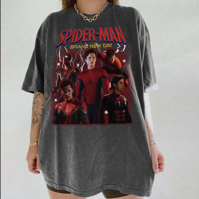 May include: Dark grey t-shirt with a Spider-Man graphic and the text "SPIDER-MAN BRAND NEW DAY". The graphic shows multiple images of Spider-Man in red and blue, with lightning bolt accents.