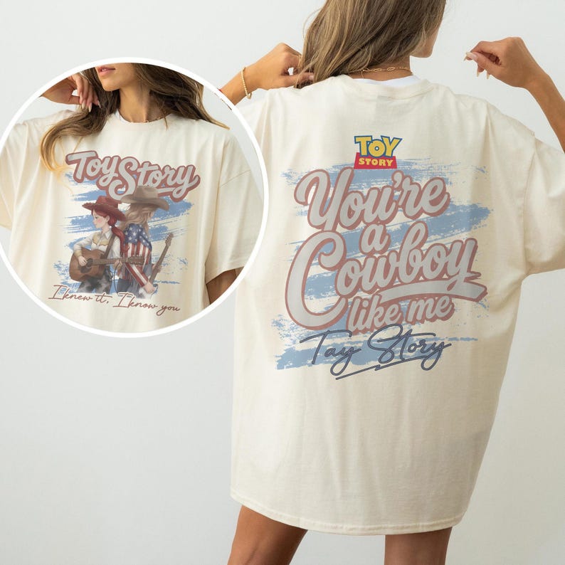 Puede incluir: Una camiseta color crema con un estampado gr&aacute;fico en la espalda con el texto Toy Story, You're a Cowboy like me y Tay Story sobre un dise&ntilde;o de pincelada azul. El gr&aacute;fico frontal muestra dos figuras con atuendo de vaquero y una guitarra.