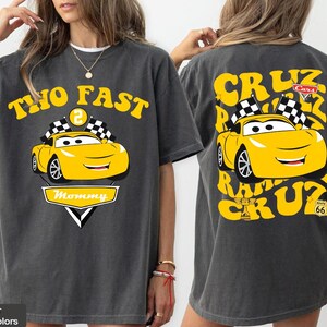 May include: Dark grey t-shirt with a yellow cartoon race car design. The front reads "TWO FAST" and "Mommy", while the back features "CRUZ" and "Route 66". The design includes checkered flags and a smiling car.