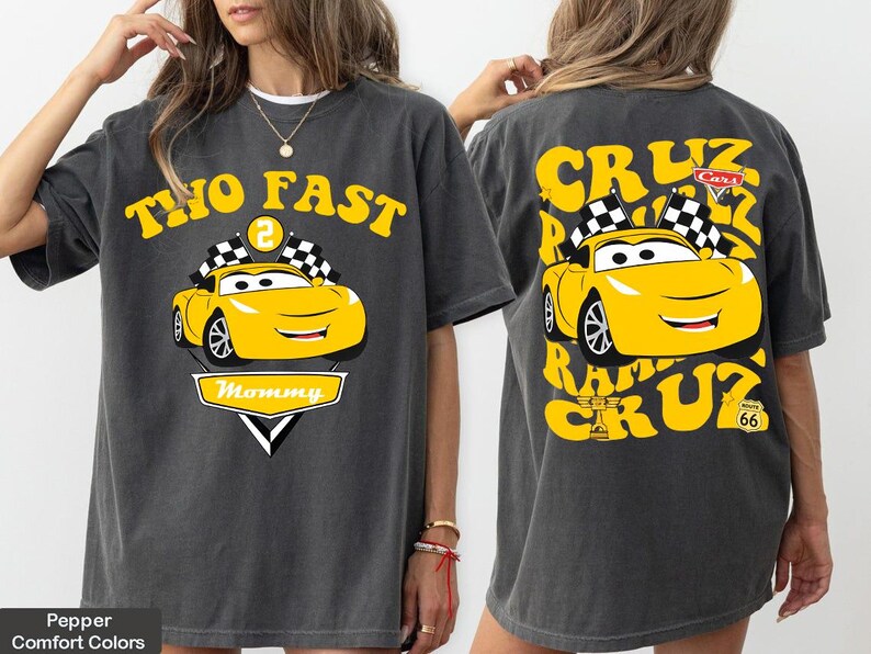 May include: Dark grey t-shirt with a yellow cartoon race car design. The front reads "TWO FAST" and "Mommy", while the back features "CRUZ" and "Route 66". The design includes checkered flags and a smiling car.