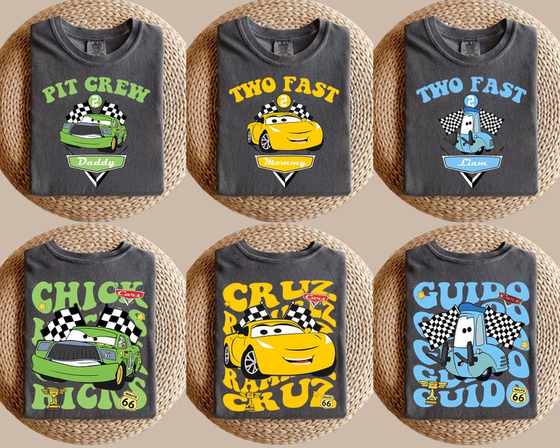 May include: Six dark grey t-shirts with car-themed designs. The shirts feature cartoon cars and text such as "PIT CREW Daddy", "TWO FAST Mommy", and "CHICK HICKS". Each design includes a racing flag and a Route 66 sign.