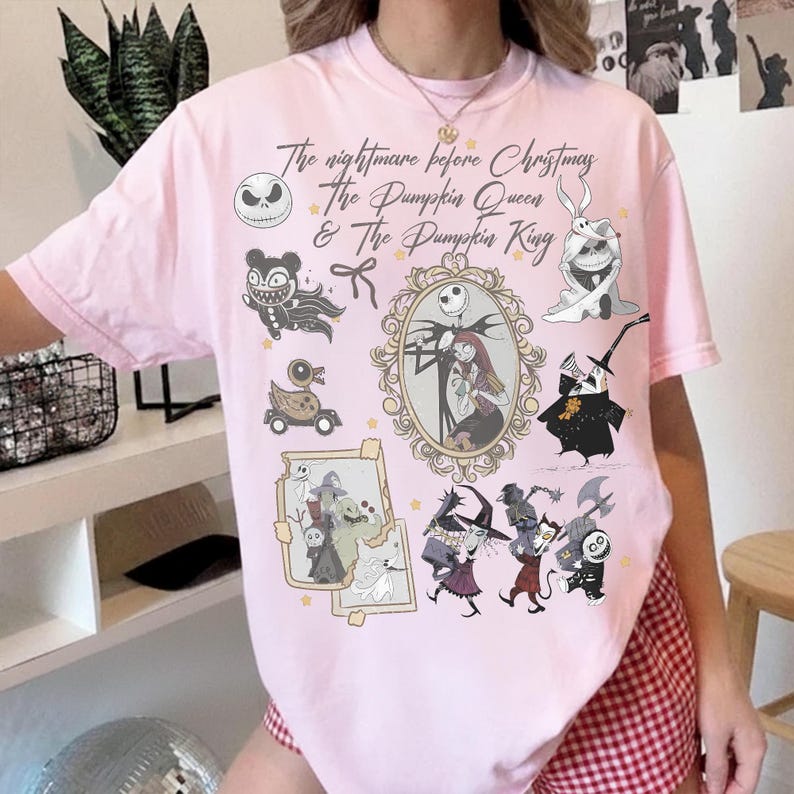 May include: A pale pink t-shirt with illustrations and text from "The Nightmare Before Christmas." The design includes Jack Skellington, Sally, and other characters in a framed portrait and other illustrations. The text reads "The Nightmare Before Christmas, The Pumpkin Queen & The Pumpkin King."