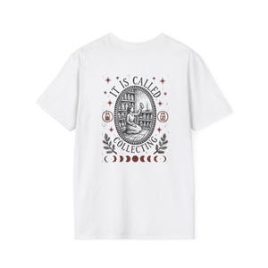 May include: A white t-shirt featuring a black and dark red graphic on the back. The design shows a person kneeling in a room with shelves of jars, surrounded by the text "IT IS CALLED COLLECTING," star icons, and a row of moon phase symbols.