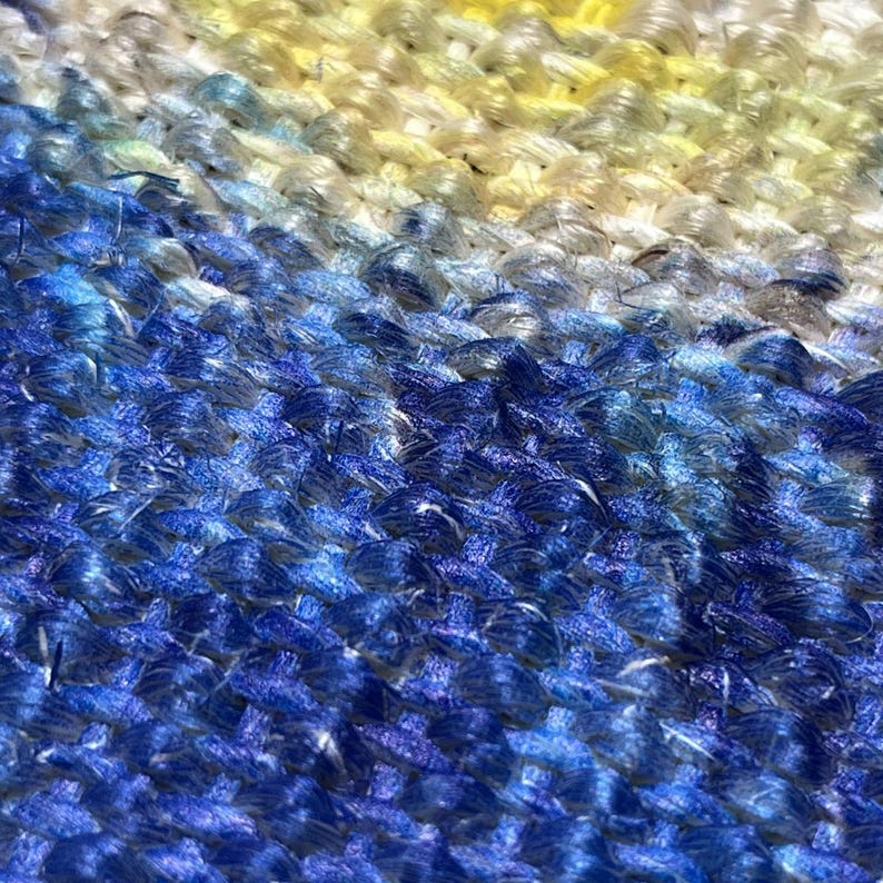 May include: A close-up view of a woven textile featuring a dense, textured pattern of interlocking threads. The color palette transitions from a bright, pale yellow at the top to a deep, vibrant royal blue at the bottom, creating a gradient effect.