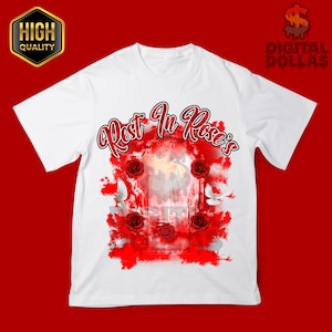 May include: White t-shirt with a graphic design featuring the text "Rest In Rose's" in red script. The design includes red roses, white doves, and a central image with a soft, blurred effect. The shirt has short sleeves.
