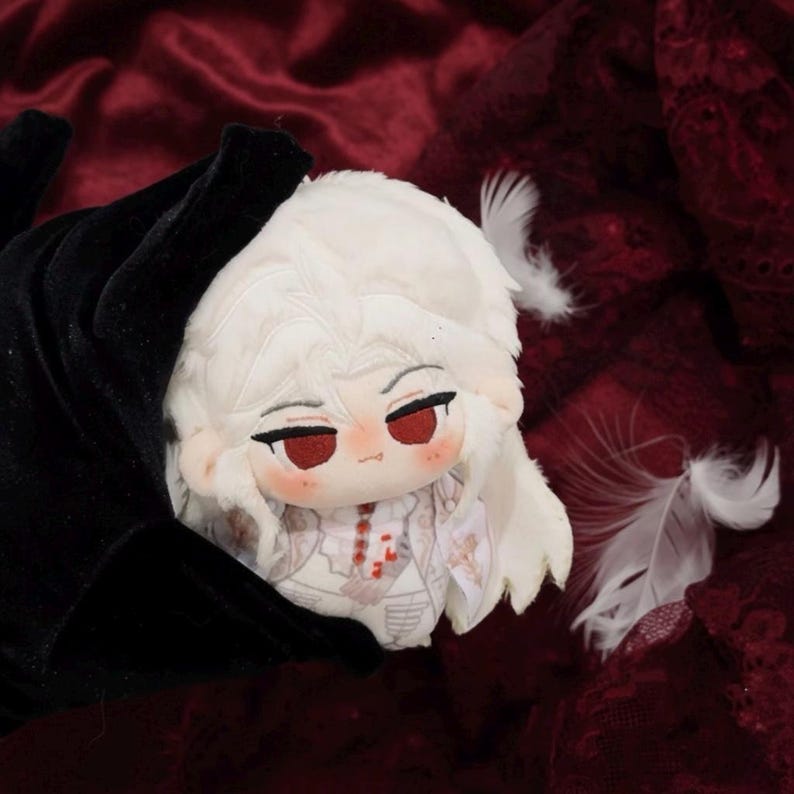 May include: A plush doll with white hair and red eyes, wearing a white and red patterned outfit. The doll is held by a black velvet glove. White feathers are scattered around the doll on a burgundy fabric.